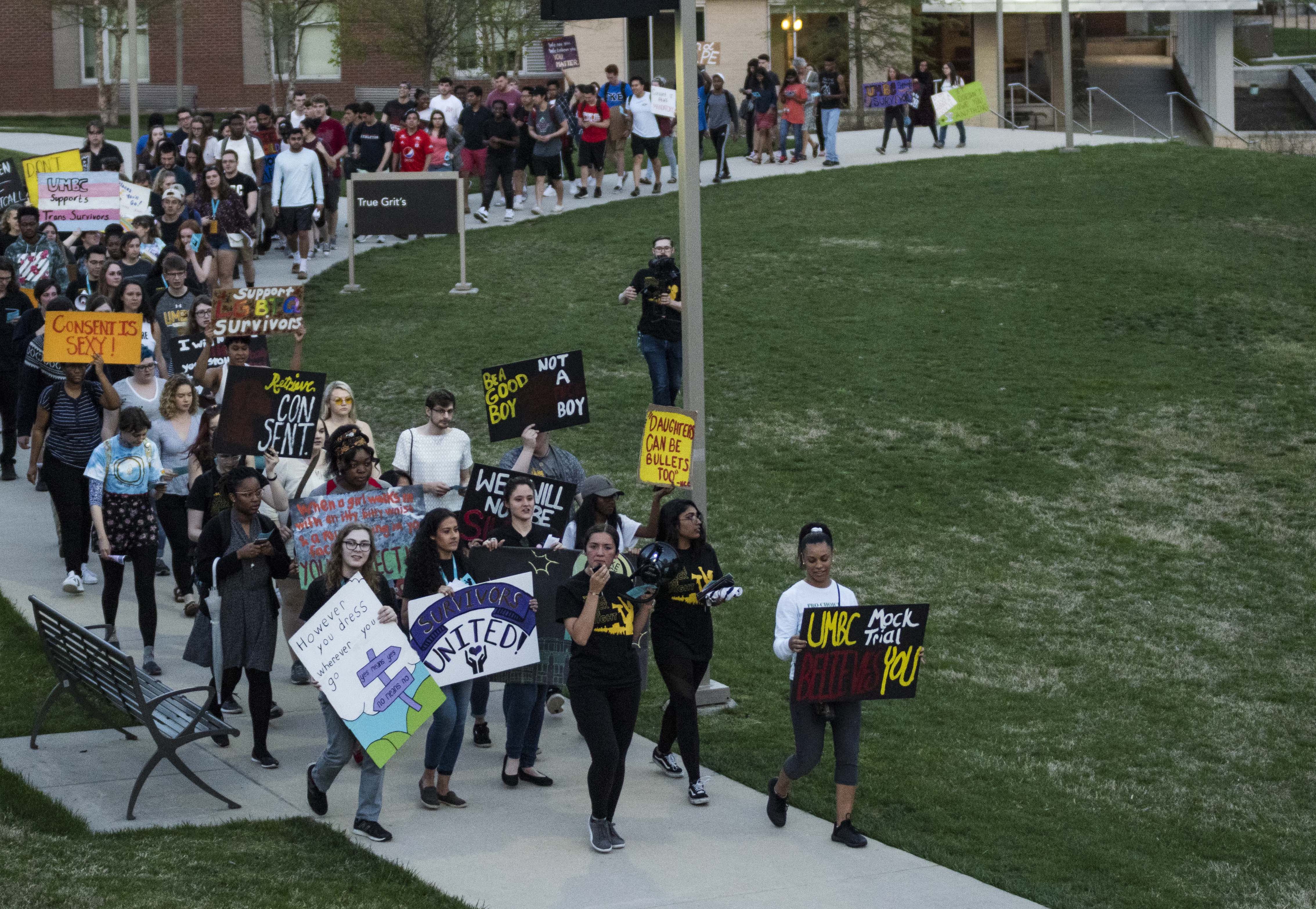 About 150 students march on the curved sidewalk in front of True Grit’s holding protest signs with pro-consent messages. 