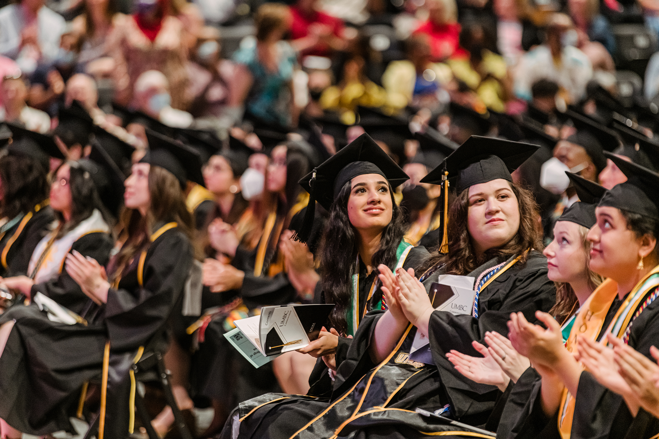 UMBC commencement with a diverse group of young women standing together in the crowd