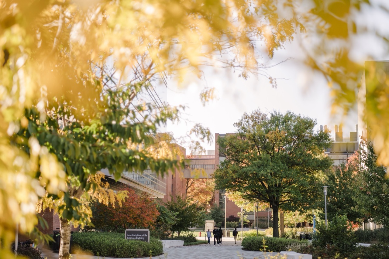 People walking on a pathway toward a building in fall, a sign reads "Interdisciplinary Life Sciences Building."